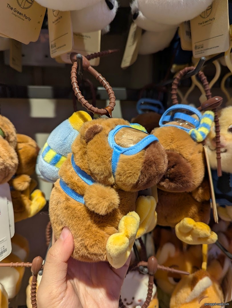Hand holding a brown plush toy keychain in a shop.