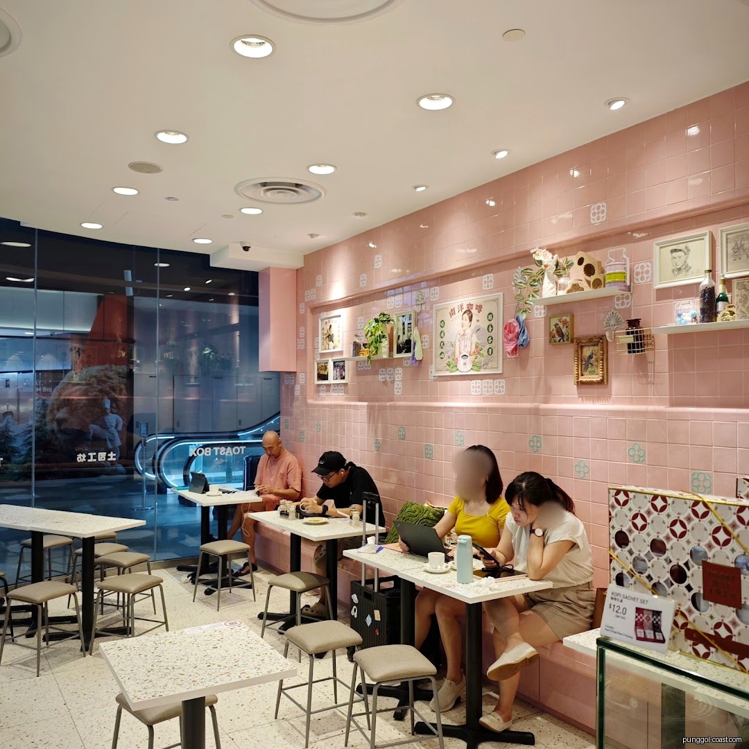 Customers seated inside a pink-walled cafe with tables and chairs.