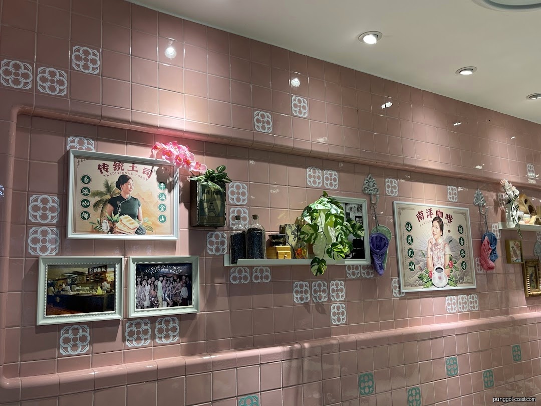 Pink tiled wall with framed pictures, plants, and decorative items inside a shop.