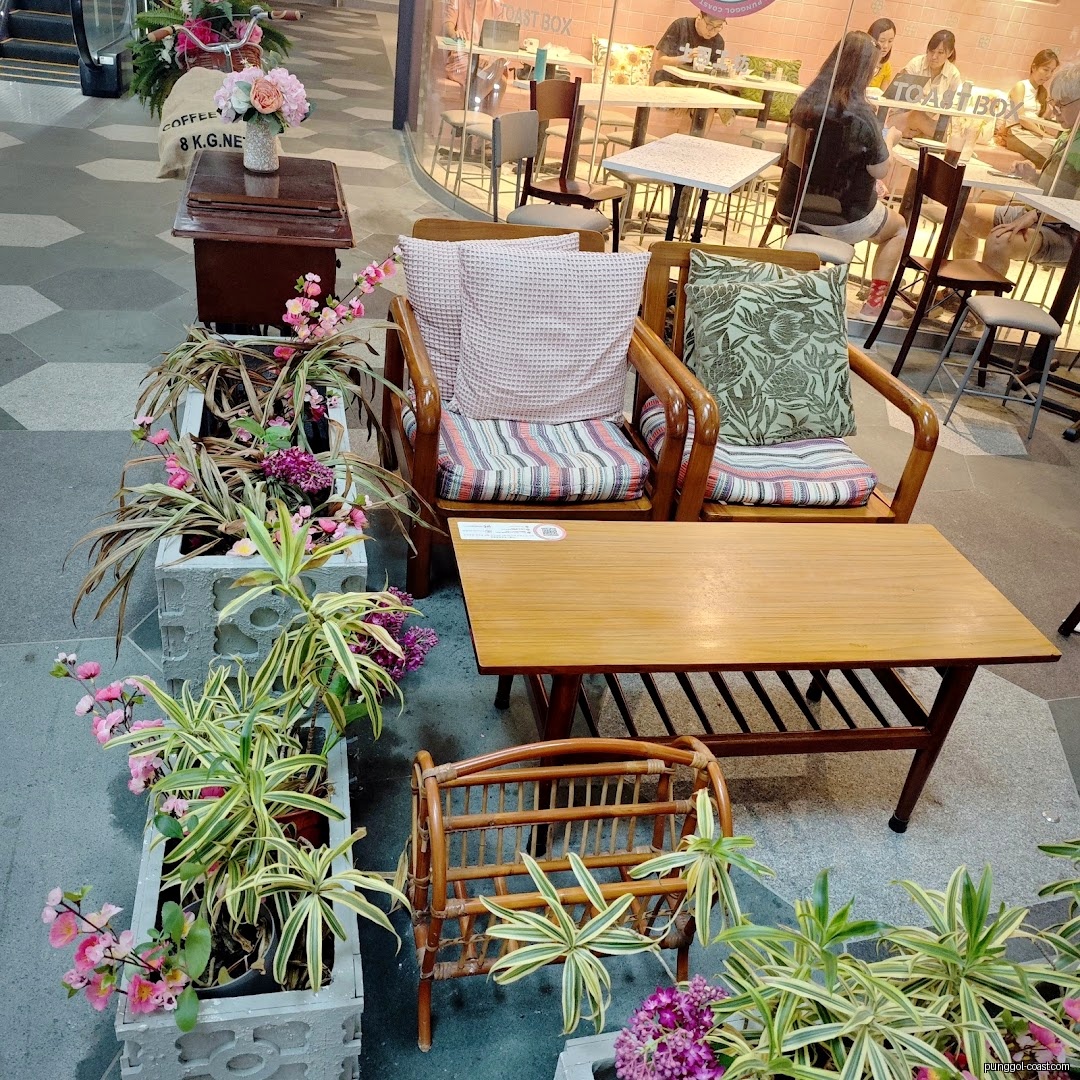 Outdoor seating and plants next to Toast Box shop interior.