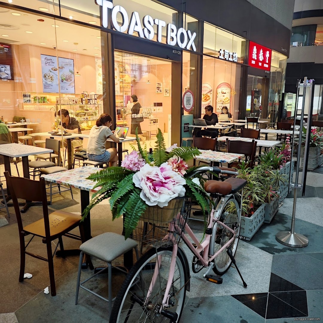 Toast Box shop front with outdoor seating, customers, and a pink bicycle.
