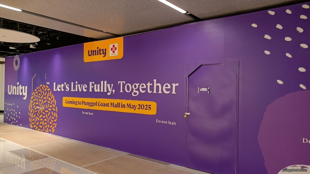 Purple hoarding for Unity shop announcing its May 2025 opening at Punggol Coast Mall.