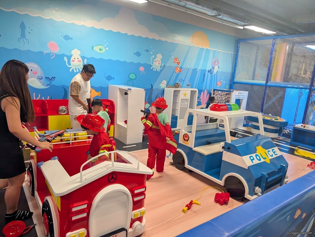 Children and adults playing in an indoor ocean-themed play area with toy vehicles.