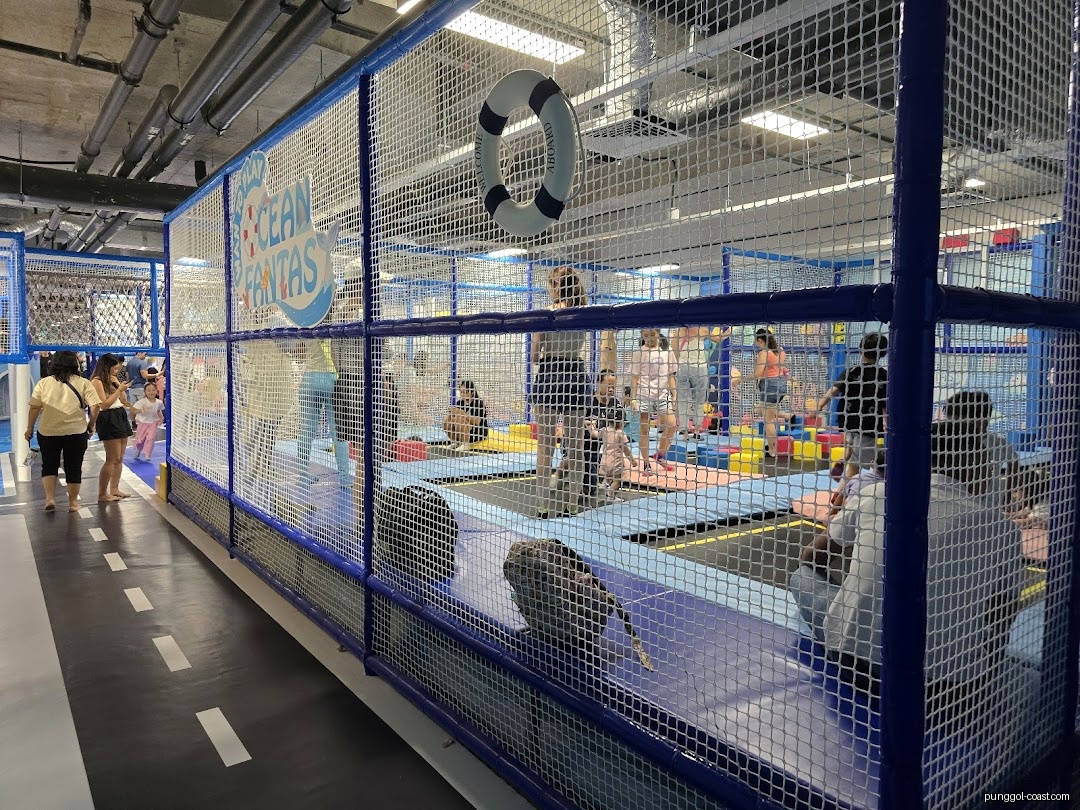 Indoor play area with trampolines and people, enclosed by netting.