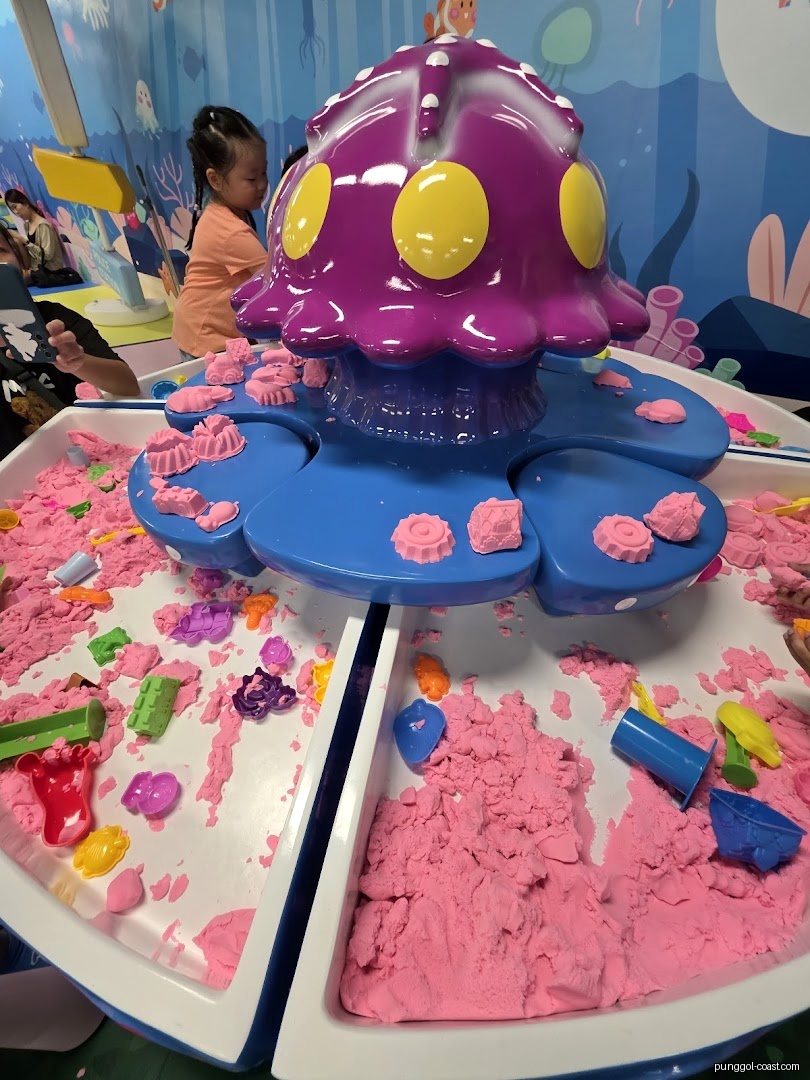 Indoor play area with pink kinetic sand, toys, and a child.