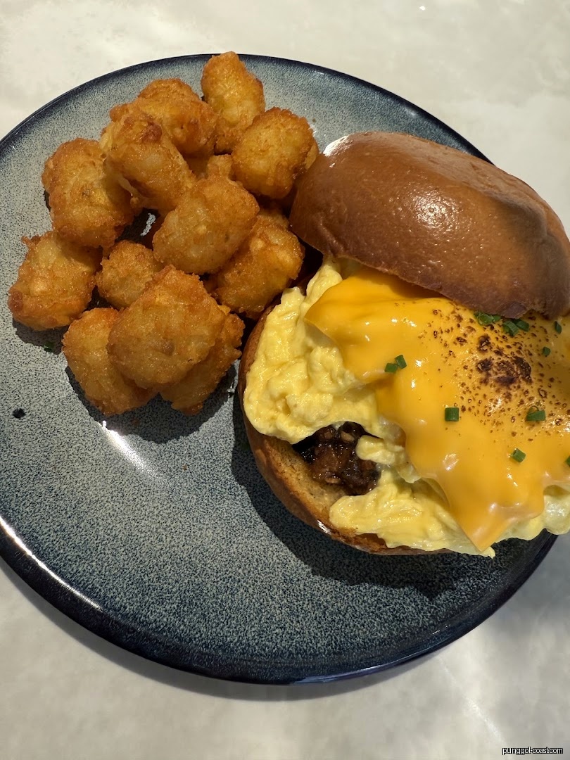 A plate with a breakfast sandwich (eggs, cheese) and a side of tater tots.