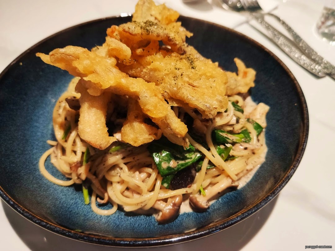 Spaghetti with mushrooms, greens, and crispy fried topping in a blue bowl.