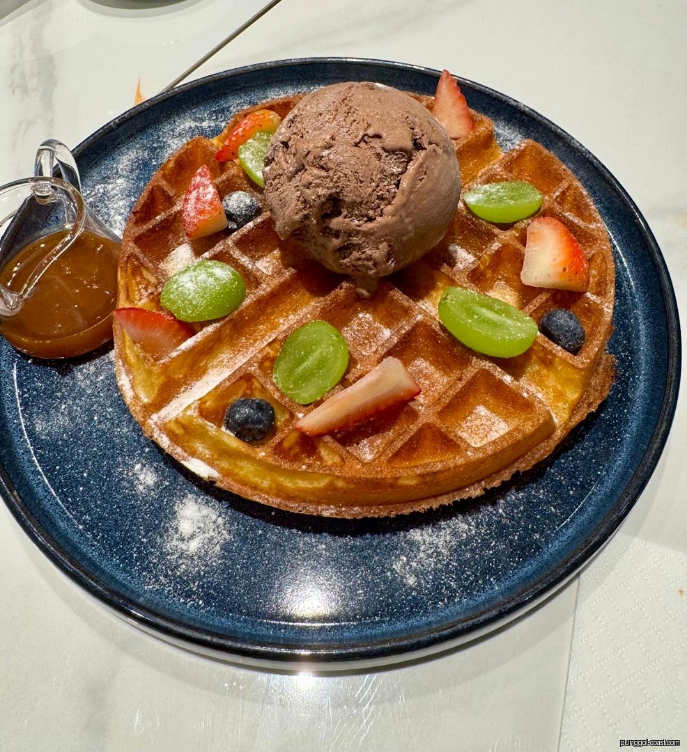 Waffle with chocolate ice cream, fresh fruit, and syrup on a blue plate.