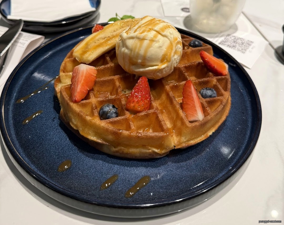Waffle with ice cream, strawberries, blueberries, and banana on a blue plate.