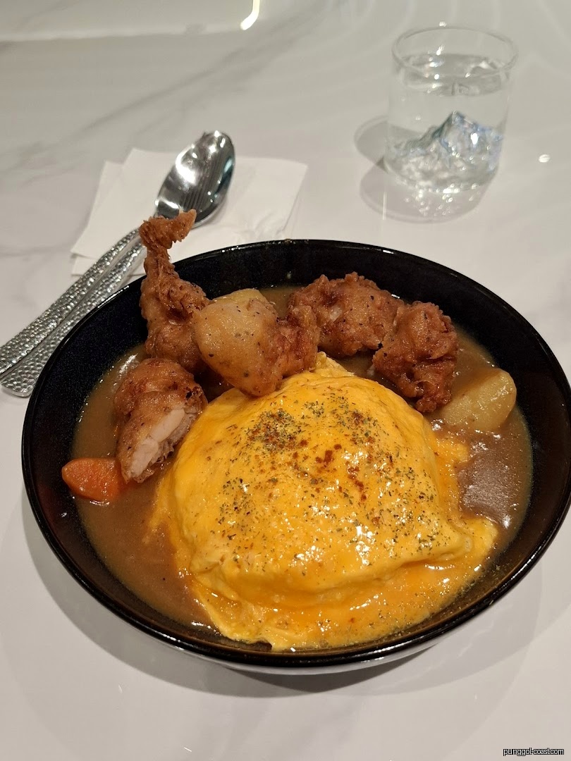 A bowl of omelet rice with fried chicken and curry, spoon, and water.