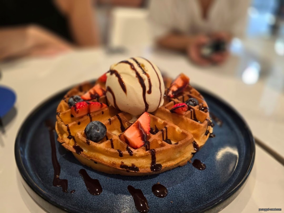 A waffle with ice cream, berries, and chocolate drizzle on a blue plate.