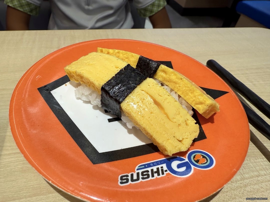 Two pieces of tamago sushi on an orange plate with chopsticks.