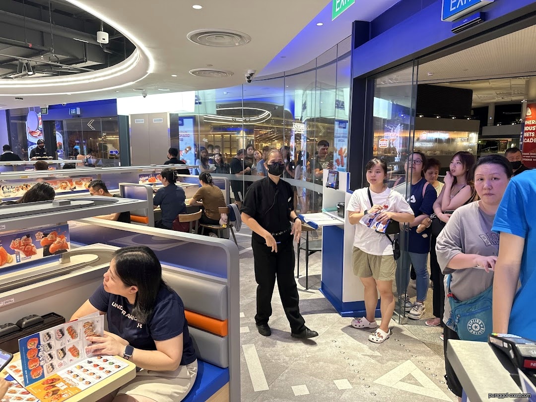 Customers dining inside a busy restaurant, with people waiting in line.