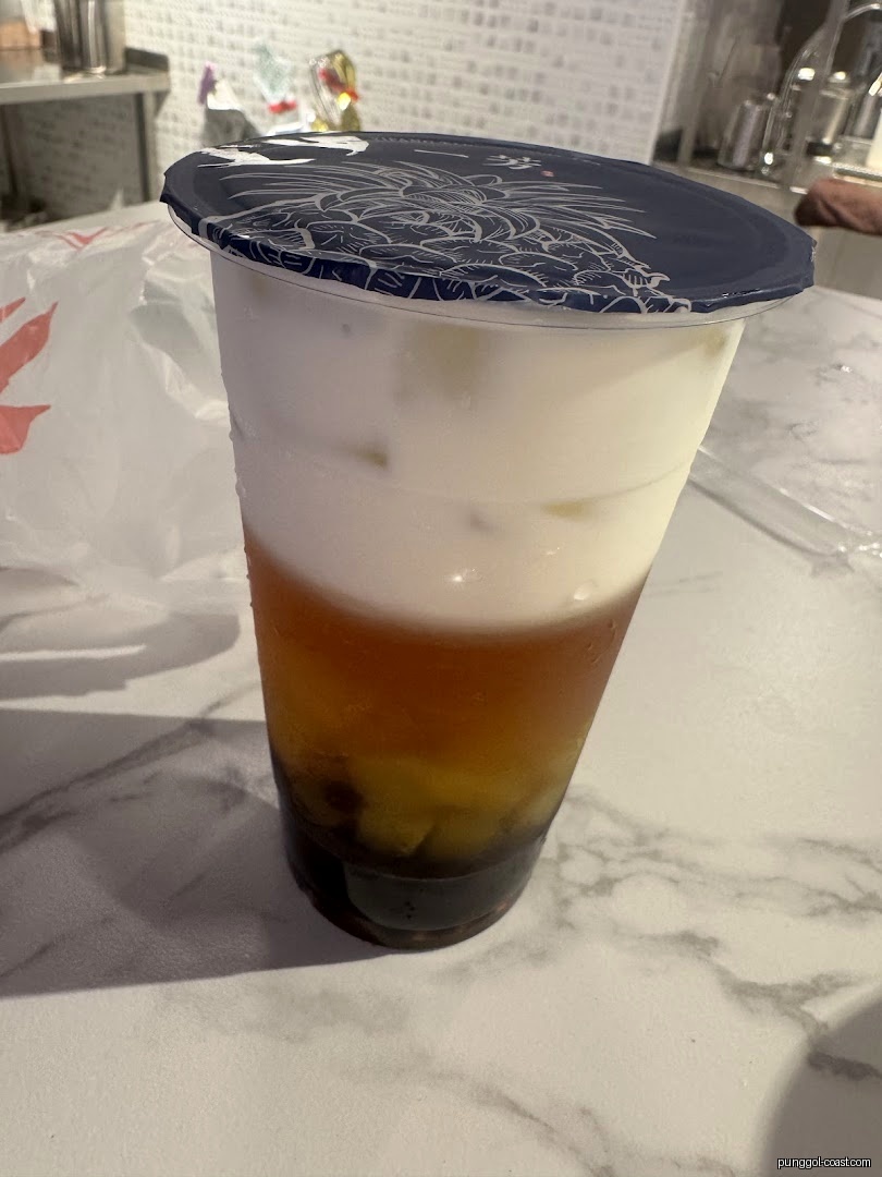 A layered drink in a plastic cup with a sealed lid on a counter.