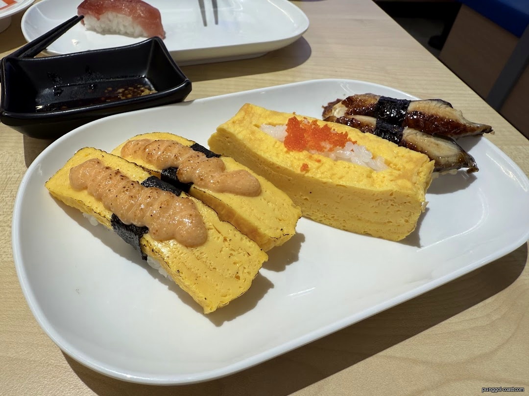 A white plate with various sushi, including tamagoyaki and unagi, on a table.