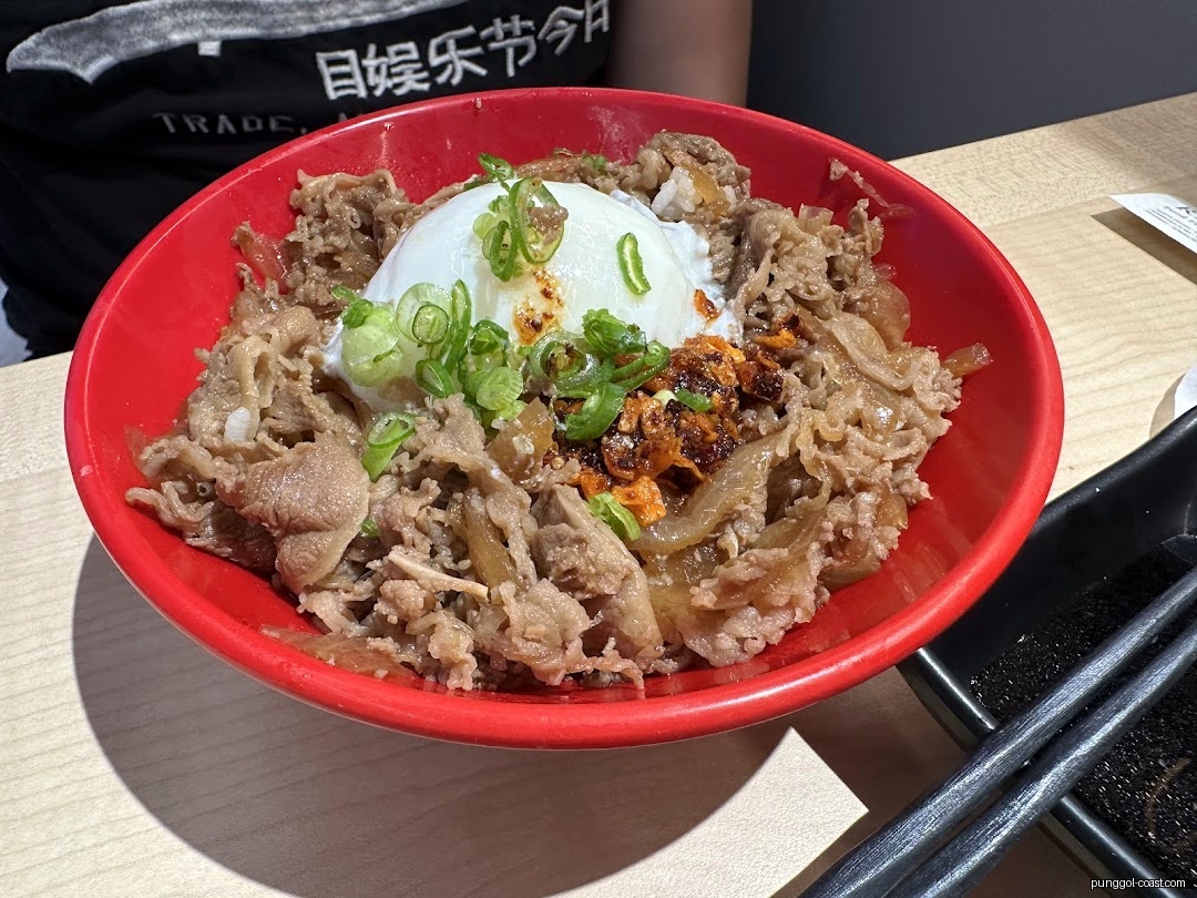 A red bowl of beef donburi with a poached egg and green onions.
