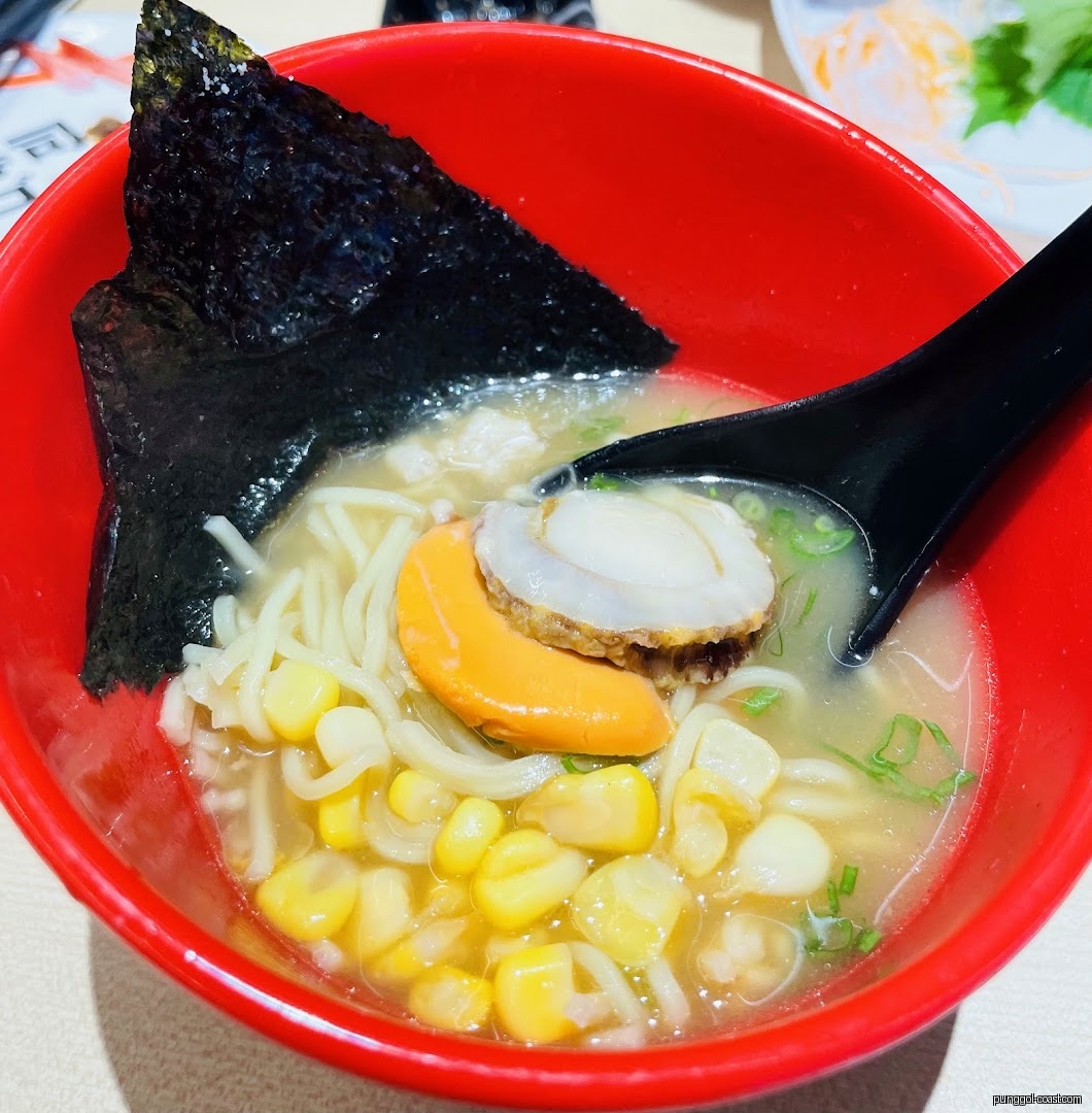 Close-up of a bowl of noodles with seafood, corn, and seaweed.