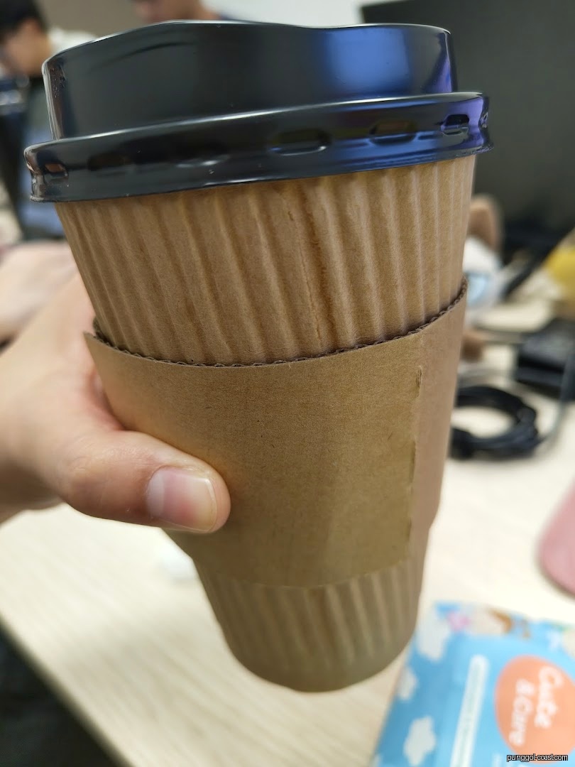 Hand holding a brown disposable cup with a black lid.