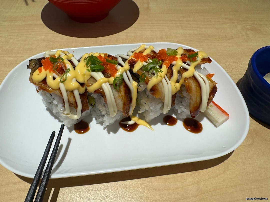 Sushi rolls with eel, sauces, and roe on a white plate with chopsticks.