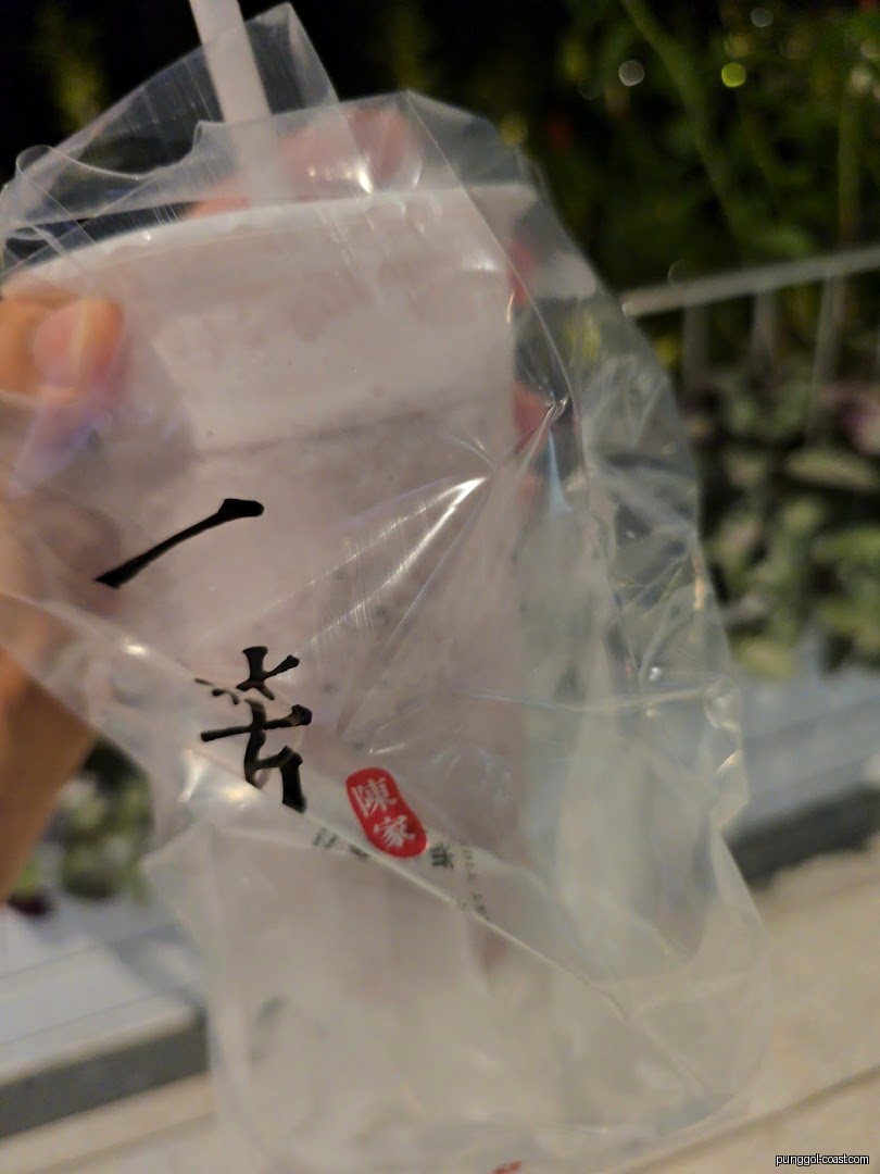Hand holding a bubble tea drink in a plastic bag with a straw.