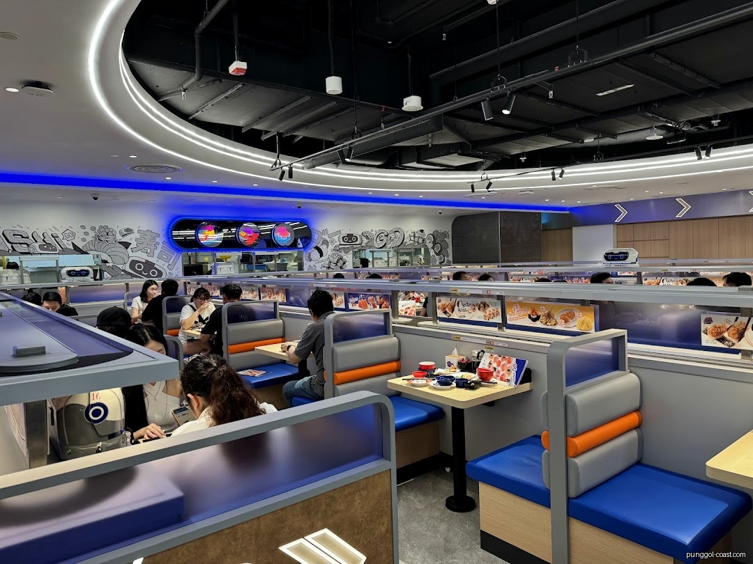 Interior of a busy sushi restaurant with customers and a conveyor belt.