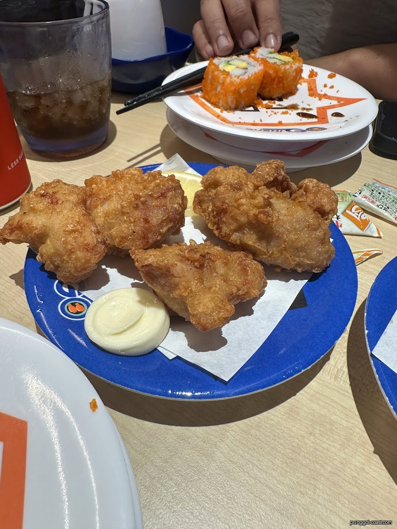 Plates of fried chicken and sushi on a table with a drink.