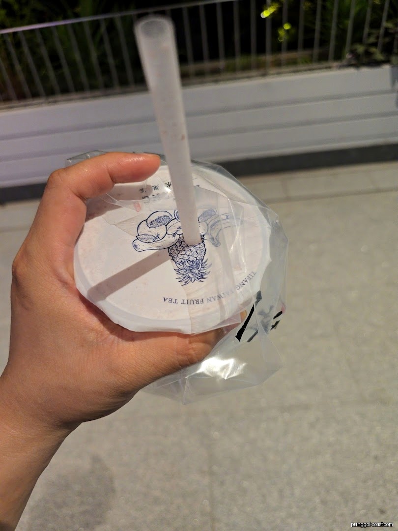 A hand holds a Yi Fang Taiwan Fruit Tea cup with a straw.